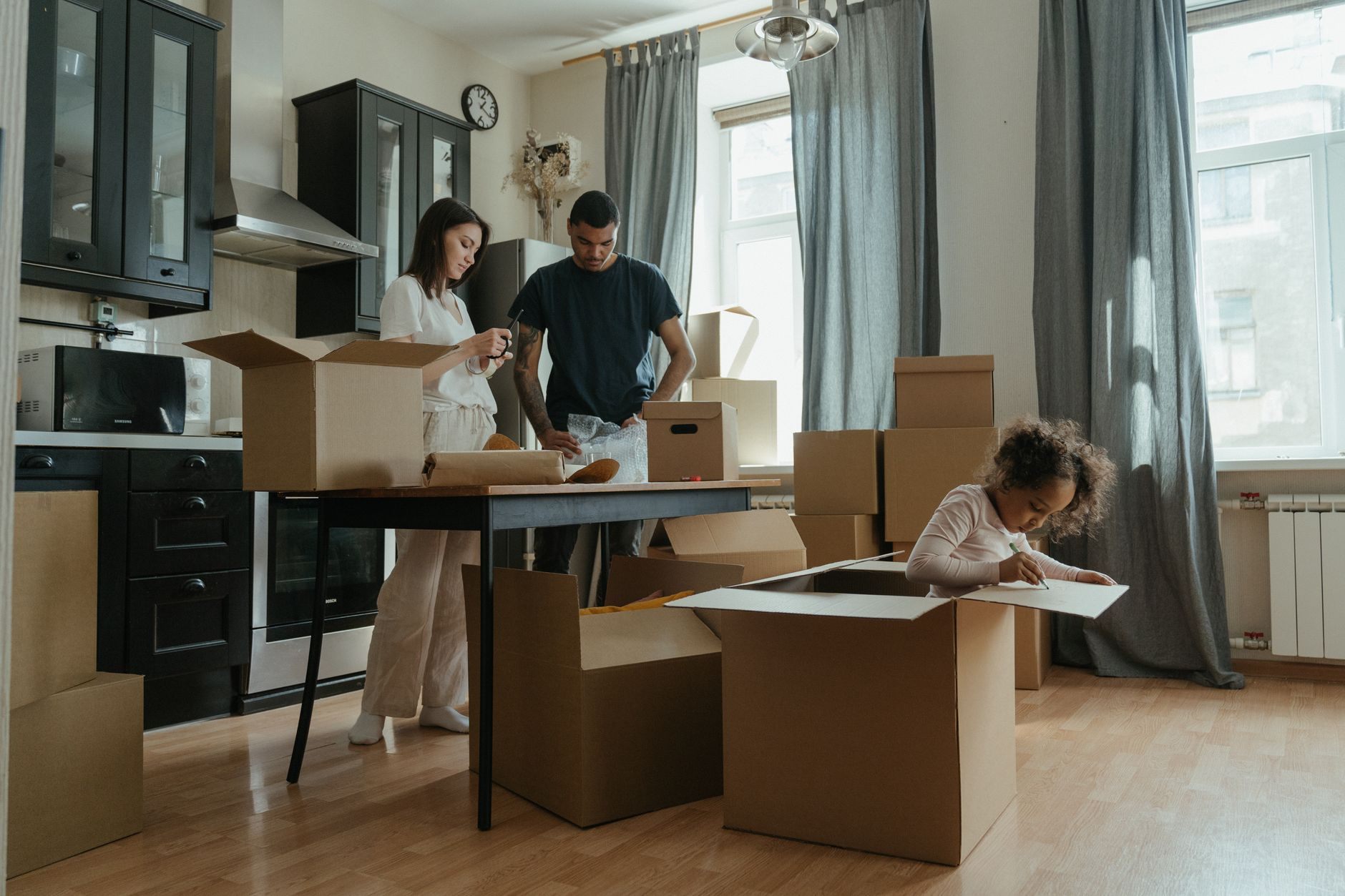 Adult children packing up dishes and kitchenware into moving boxes while clearing out a parent's longtime home