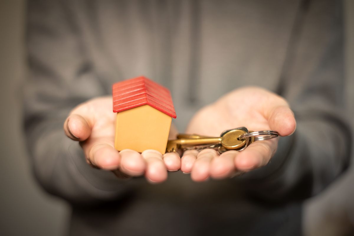 Hands holding out house keys and a small model house