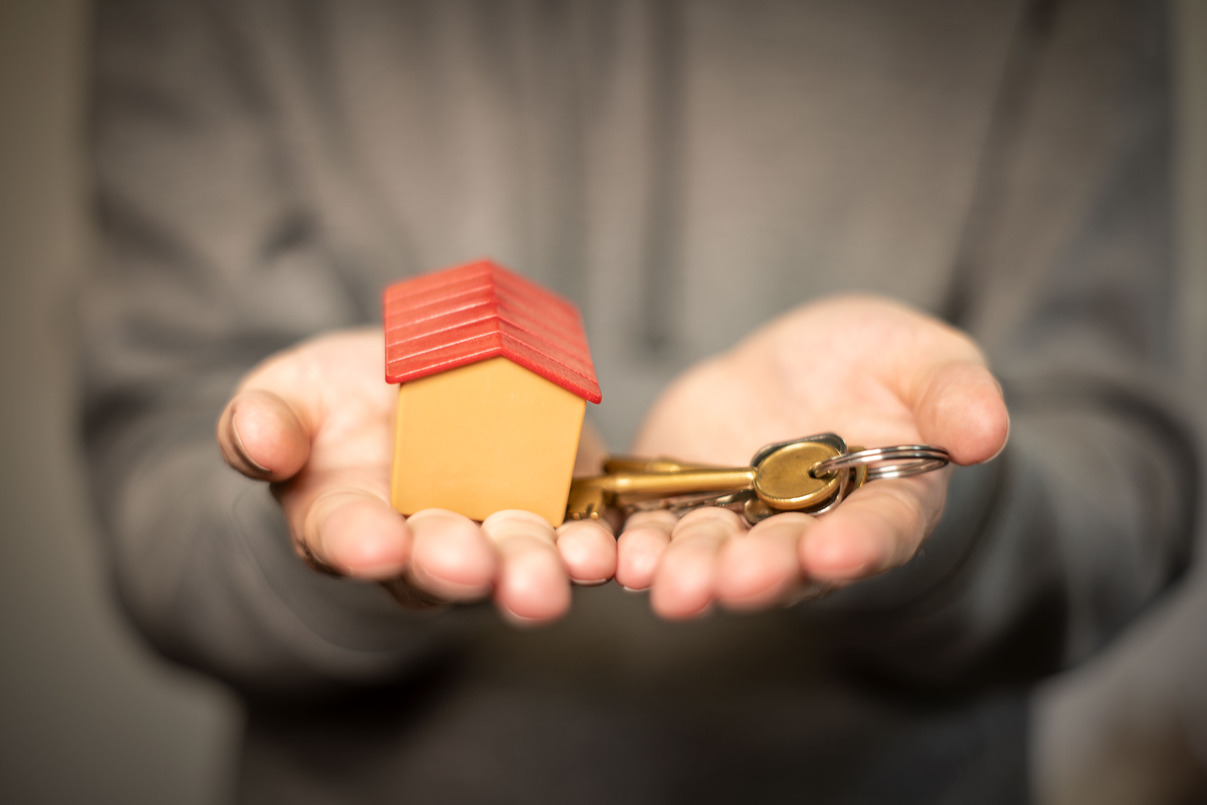 Hands holding out house keys and a small model house