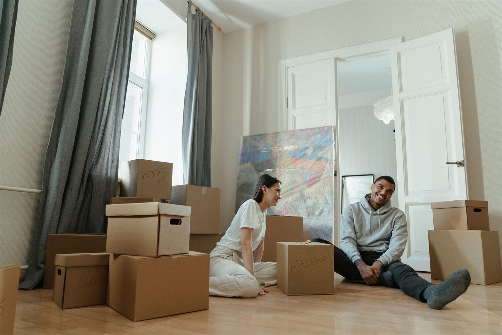 Couple sitting among moving boxes in the bright living room of their new home