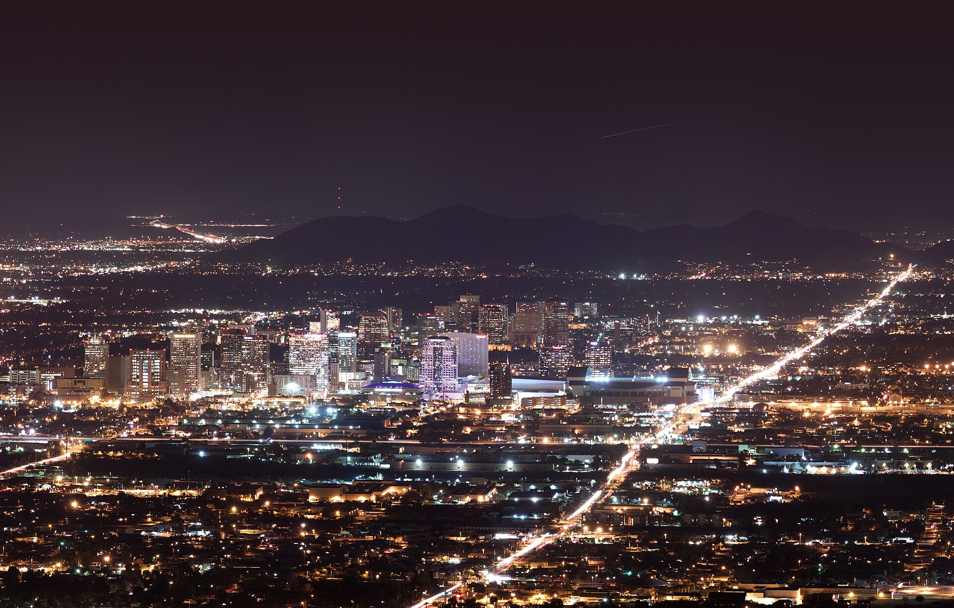Downtown Phoenix skyline lit up at night with mountains behind