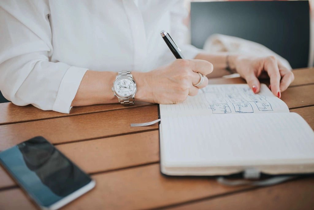 Person working through numbers in a notebook at a wooden table